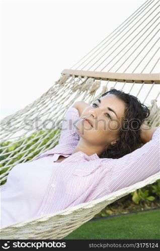 Portrait of pretty young adult Caucasian brunette female lying in hammock relaxing.
