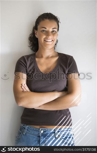 Portrait of pretty young adult Caucasian brunette female with arms crossed smiling and looking at viewer.