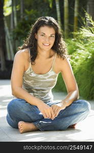 Portrait of pretty young adult Caucasian brunette woman sitting indian style smiling and looking at viewer.