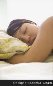 Portrait of pretty young Asian woman lying in bed with head on pillow with eyes closed.