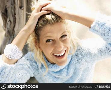 Portrait of pretty young blond woman sitting on beach in Maui, Hawaii smiling and holding back hair with hands.