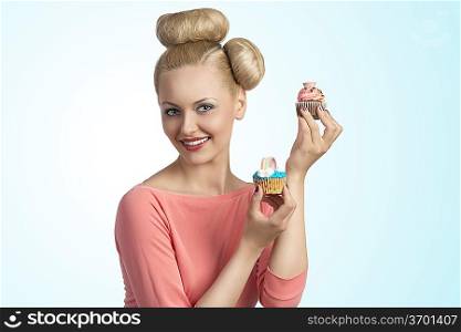 portrait of pretty young girl with funny hair-style and colourful make-up taking two cupcakes in the hands and smiling
