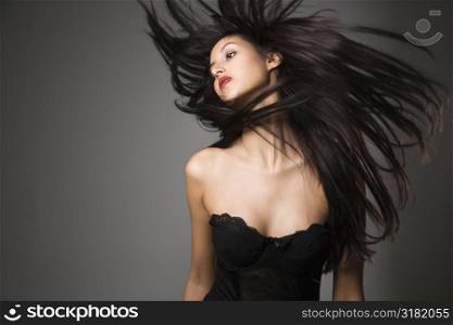 Portrait of pretty young woman flinging long black hair into air.
