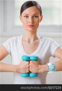 Portrait of pretty young woman wearing smart watch device while lifting dumbbells