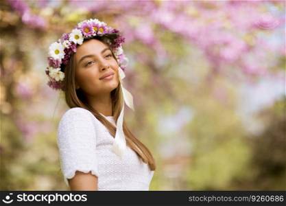 Portrait of pretty young woman with wreath of fresh flowers on head in the park