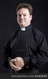 Portrait of priest holding a bible. Black background.