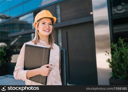 Portrait of professional architect woman wearing yellow helmet and looking at modern building outdoors. Engineer and architect concept.
