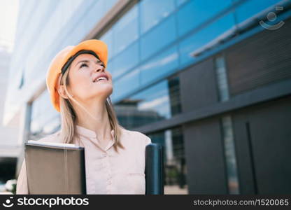 Portrait of professional architect woman wearing yellow helmet and looking at modern building outdoors. Engineer and architect concept.