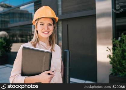 Portrait of professional architect woman wearing yellow helmet and looking at modern building outdoors. Engineer and architect concept.