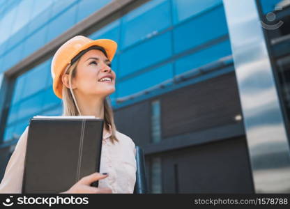 Portrait of professional architect woman wearing yellow helmet and looking at modern building outdoors. Engineer and architect concept.