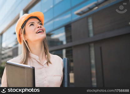 Portrait of professional architect woman wearing yellow helmet and looking at modern building outdoors. Engineer and architect concept.