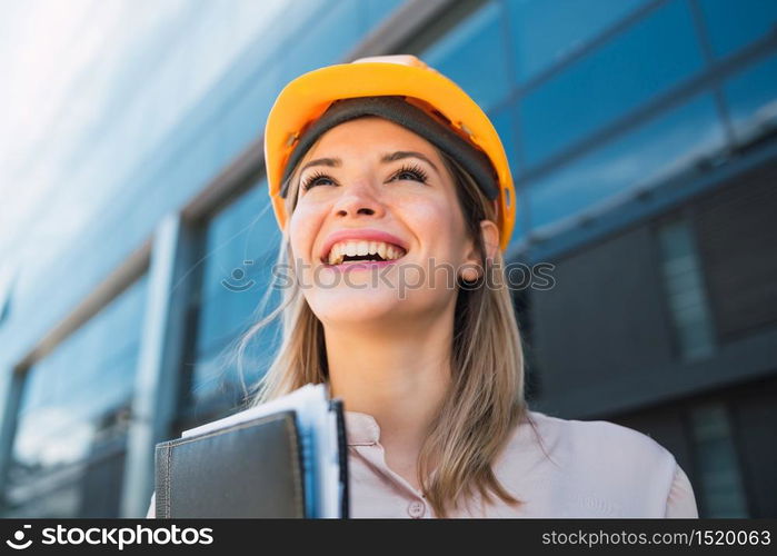 Portrait of professional architect woman wearing yellow helmet and standing outdoors. Engineer and architect concept.