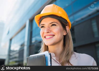 Portrait of professional architect woman wearing yellow helmet and standing outdoors. Engineer and architect concept.