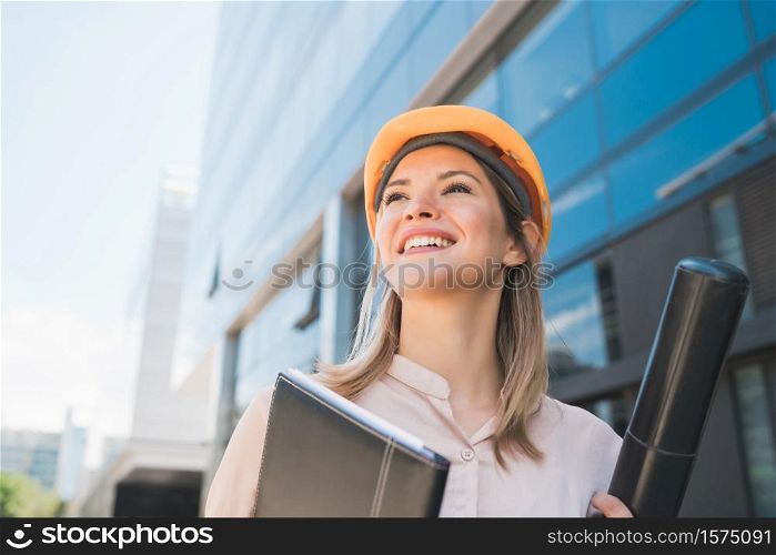 Portrait of professional architect woman wearing yellow helmet and standing outdoors. Engineer and architect concept.