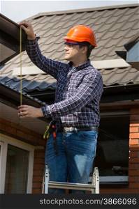 Portrait of professional worker measuring height of roof with tape