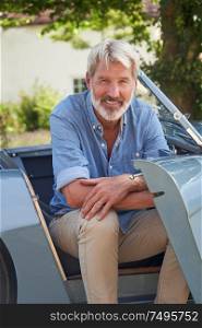 Portrait Of Proud Mature Man Sitting In Restored Classic Sports Car Outdoors At Home