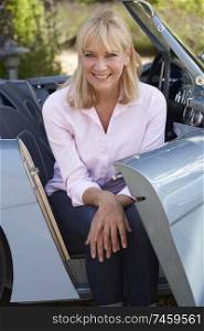 Portrait Of Proud Mature Woman Sitting In Restored Classic Sports Car Outdoors At Home                             