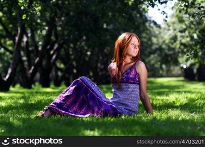 Portrait of red-haired beautiful young woman, against green of summer park.