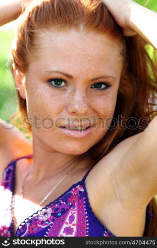 Portrait of red-haired beautiful young woman, against green of summer park.