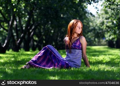 Portrait of red-haired beautiful young woman, against green of summer park.