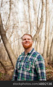 Portrait of red haired man with plaid shirt and long beard in the forest