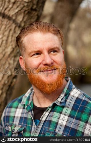 Portrait of red haired man with plaid shirt and long beard in the forest