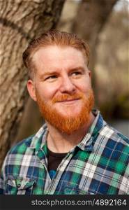 Portrait of red haired man with plaid shirt and long beard in the forest