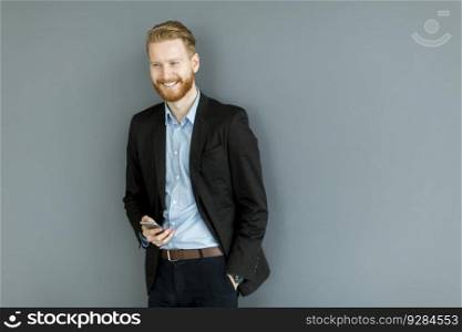 Portrait of redhair man using mobile phone standing by the wall