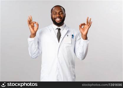Portrait of relieved and happy african-american handsome doctor in white coat, close eyes showing okay, perfection sign with pleased smile, scientist finally discover covid19 vaccine in laboratory.. Portrait of relieved and happy african-american handsome doctor in white coat, close eyes showing okay, perfection sign with pleased smile, scientist finally discover covid19 vaccine in laboratory