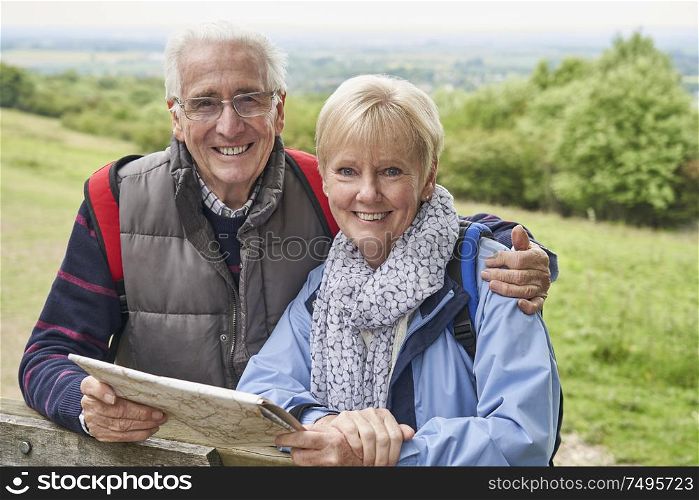 Portrait Of Retired Couple On Walking Holiday Resting On Gate With Map