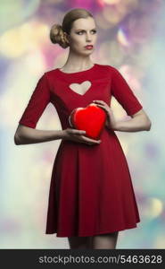 portrait of romantic blonde woman with creative hair-style and red sexy dress taking in the hands one box of chocolates