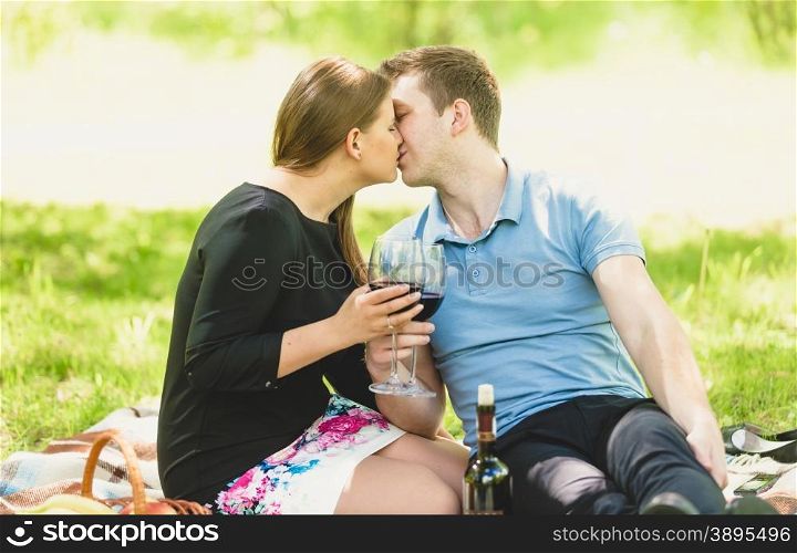 Portrait of romantic couple kissing and drinking wine at picnic