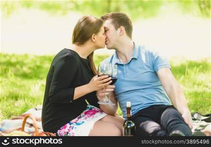 Portrait of romantic couple kissing and drinking wine at picnic