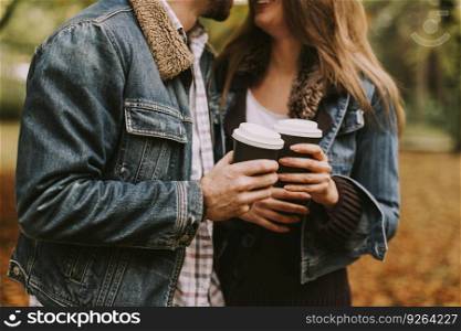 Portrait of romantic couple with coffee walking outdoors in the autumn park