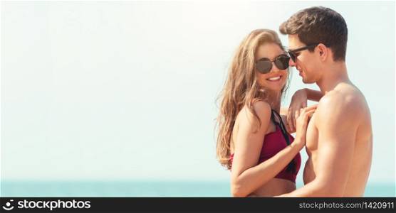 Portrait of Romantic Young couple wear sun glasses embracing together at the beach. Happy smiling Handsome man in swimwear and Beautiful woman in bikini in love at outdoor with copy space. Lover, dating.
