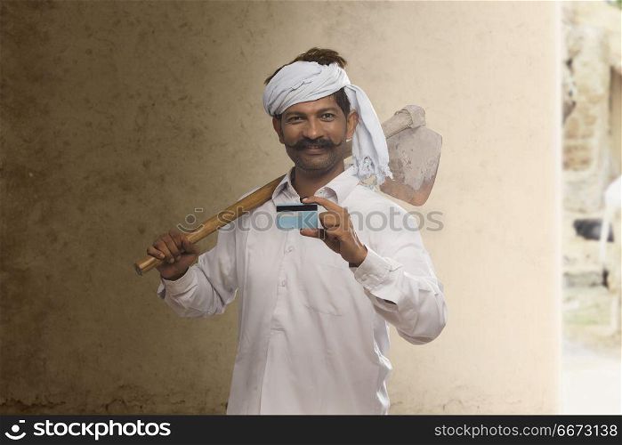 Portrait of rural farmer holding credit card and carrying hoe on his shoulder