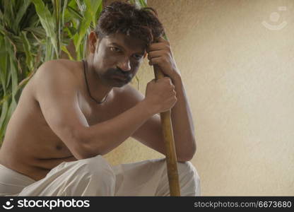 Portrait of rural farmer holding hoe sitting against crops