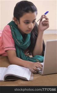 Portrait of rural girl lying on floor using laptop and studying