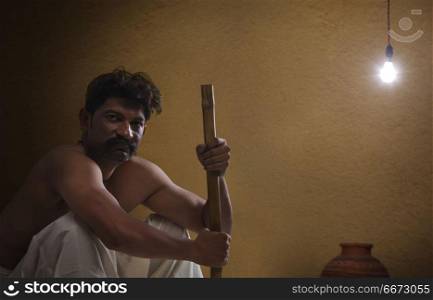 Portrait of rural Indian man sitting indoors holding stick