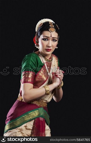 Portrait of sacred Bharatanatyam dancer performing over black background