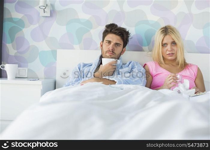 Portrait of sad couple holding coffee mug and glass while relaxing on bed