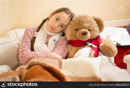 Portrait of sad girl with flu lying in bed with teddy bear