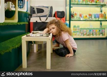 Portrait of sad little girl sitting nearby big steel feed bowl dreaming about dog. Pet shop interior. Sad little girl sitting nearby big feed bowl dreaming about dog at pet shop