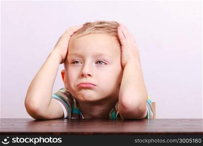 Portrait of sad unhappy tired blond boy. Child kid making silly funny face at the table interior. Emotions.