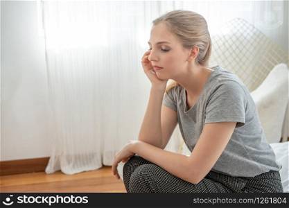 Portrait of sad upset worry and depressed young caucasian woman sit on bed in home with sorrow,hopeless,unhappy in trouble emotion.