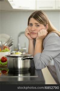 Portrait of sad woman leaning on table at kitchen while cooking