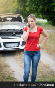 Portrait of sad woman standing at broken car at rural road and calling for help