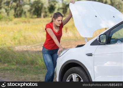 Portrait of sad woman standing at broken car with open hood
