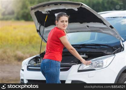Portrait of sad woman standing at broken car with open hood