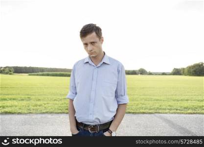 Portrait of sad young man with hands in pockets standing on rural road